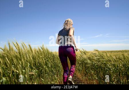 Laufen im Weizen Junges Mädchen, das im Spätsommer durch Weizenfeld läuft. Stockfoto