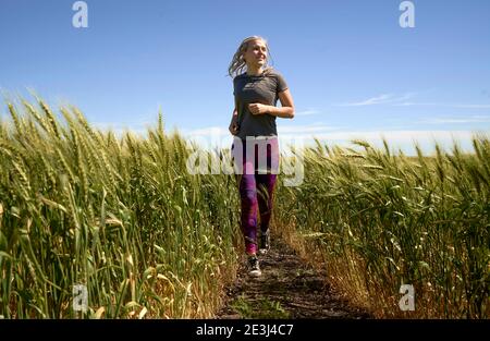 Laufen im Weizen Junges Mädchen, das im Spätsommer durch Weizenfeld läuft. Stockfoto