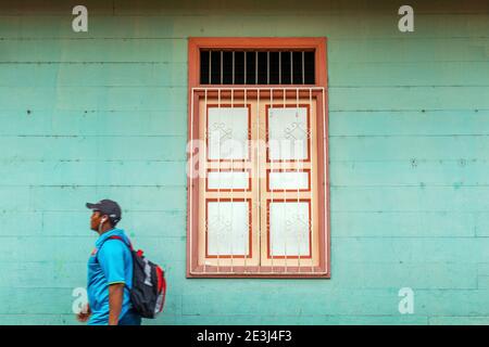 Junger ecuadorianischer Mann mit Ohrhörern, der an kolonialer Fensterarchitektur in Guayaquil, Ecuador vorbeikommt. Stockfoto