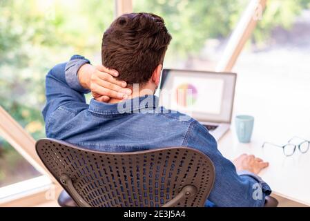 Rückansicht eines unerkennbaren Geschäftsmannes, der hinter seinem Laptop sitzt und starke Kopfschmerzen hat. Stockfoto