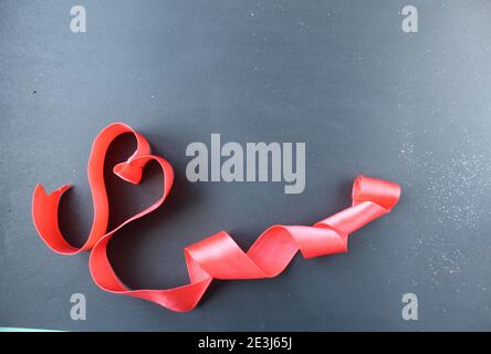 Rotes Herz von Band mit Locken auf schwarzem grauen Hintergrund mit Copyspace Platz für Text valentinstag. Stockfoto