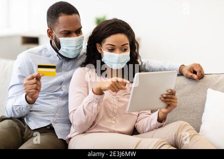 Schwarzes Paar in medizinischer Maske mit Tablet und Kreditkarte Stockfoto