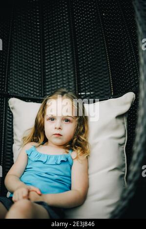 Kleines Mädchen schwingt in einem Hängesessel.das Baby. Kleines Mädchen auf einer Schaukel mit Rattan Stockfoto