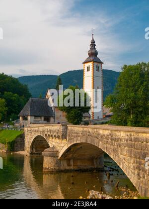 Kirche-Turm und Stein Brücke am Bohinj See im Bergdorf Ribicev Laz, Slowenien Stockfoto