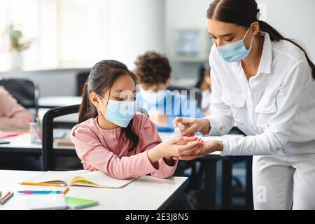 Lehrer, der antibakterielle Desinfektionsmittel auf die Hände der Schüler anwendet Stockfoto