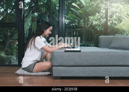 Schöne asiatische Frau lächelnd und Blick auf Laptop im Wohnzimmer. Arbeiten, Lernen von zu Hause Konzept. Stockfoto