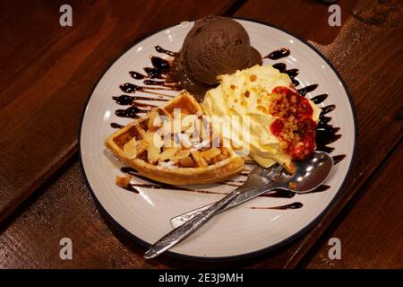 Süße Waffel mit Schlagsahne, Erdbeersirup und Schokoladeneis Sahne Belag Walnuss Honig und Schokolade Rezept auf Keramikplatte Teller im Cafe coff Stockfoto