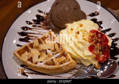 Süße Waffel mit Schlagsahne, Erdbeersirup und Schokoladeneis Sahne Belag Walnuss Honig und Schokolade Rezept auf Keramikplatte Teller im Cafe coff Stockfoto