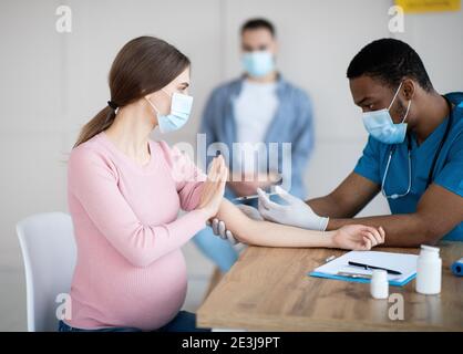 Schwangere Dame, die den Arzt davon abhält, einen covid-19-Impfstoffschuss zu machen, um die Coronavirus-Immunisierung in der Klinik zu bekämpfen Stockfoto