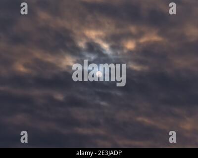 Wunderschöne Aussicht auf den dramatischen Himmel mit runder Sonne in der Mitte, die in der Wintersaison durch orangefarbene dunkle Wolken scheint. Von Wurmlingen aus gesehen. Stockfoto