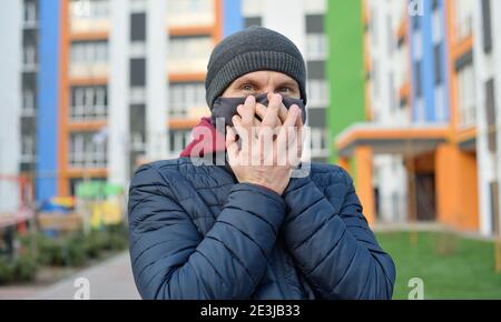 Schöner junger Europäer in Winterkleidung auf der Straße mit einer medizinischen Gesichtsmaske. Nahaufnahme eines 35-jährigen Mannes in einer Atemschutzmaske zum Schutz vor Stockfoto