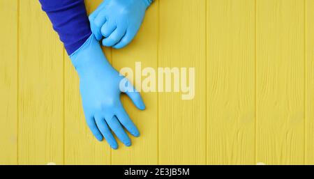 Banner blaue Nitrilhandschuhe. Hände eines Sanitäter in den blauen Latexhandschuhen auf einem gelben Holzhintergrund mit Platz für Ihren Text Stockfoto