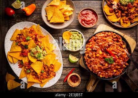 Mexikanisches Food-Konzept: Tortilla Chips, Guacamole, Salsa, Chili con Carne und frische Zutaten auf Holzhintergrund, Draufsicht Stockfoto