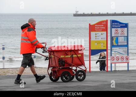 Weymouth, Dorset, Großbritannien. Januar 2021. UK Wetter: Ein Postbote, der an der Küste entlang läuft und seine Lieferungen in Weymouth in Dorset während der Covid-19 Sperre an einem bewölkten Nachmittag macht. Bild: Graham Hunt/Alamy Live News Stockfoto