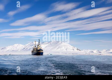 Eisbrecher vor Anker in den arktischen Gewässern von Svalbard, einem norwegischen Archipel zwischen dem Festland Norwegen und dem Nordpol. Strahlend blauer Himmel und schneebedeckter Mo Stockfoto