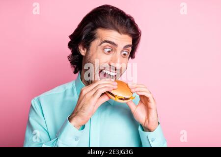 Foto Porträt des Mannes, der großen Bissen von Cheeseburger isoliert Auf pastellrosa Hintergrund Stockfoto