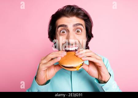 Foto-Porträt von hungrigen Mann unter massiven Bissen von Cheeseburger Isoliert auf pastellrosa Hintergrund Stockfoto