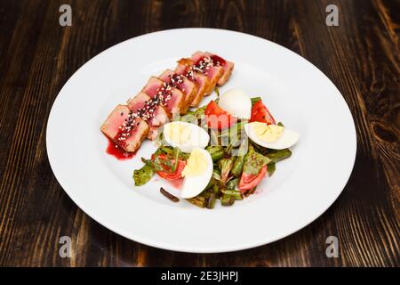 Mittelgroßes Rindersteak in Scheiben geschnitten und mit Sesamsoße auf weißem Teller beträufelt. Mit gekochtem Spargel, Eiern und Tomaten garnieren. Stockfoto