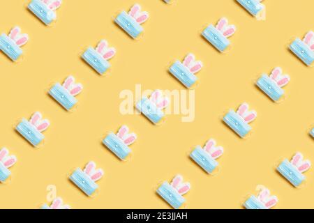 Ostern und Quarantäne. Nahtloses Muster eines Kaninchens in einer schützenden medizinischen Maske auf gelbem Hintergrund. Stockfoto