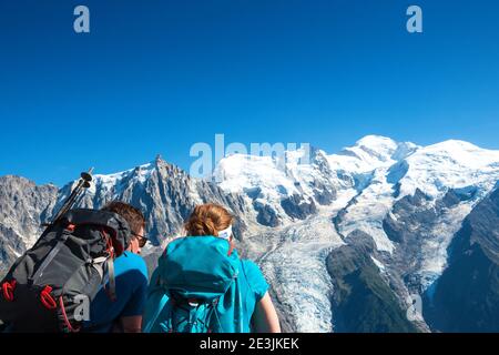 Zwei Rucksacktouristen (unerkennbares junges Paar; Rückansicht) bewundern schneebedeckten Mont Blanc Berg und Aiguille du Midi in den Alpen. Urlaub im Sommer in M Stockfoto