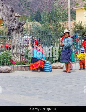 Zwei einheimische Frauen in regionalen Kostümen stehen auf dem Stadtplatz von Ollantaytambo im Heiligen Tal in Urubamba, Region Cusco, Südperu Stockfoto