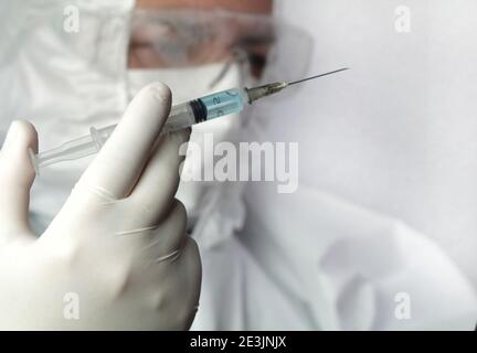 Medizinische Fachkraft mit Covid-Schutzanzug, Brille und OP-Handschuhen mit einer Spritze mit Covid-19-Virus-Impfstoff Stockfoto