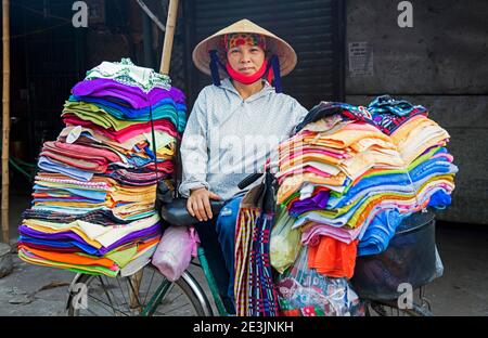 Vietnamesische Frau mit nón lá konischen Hut Verkauf Textil und Die Kleidung vom Fahrrad in der Stadt Ninh Binh in der Rotes Flussdelta im Norden Vietnams Stockfoto