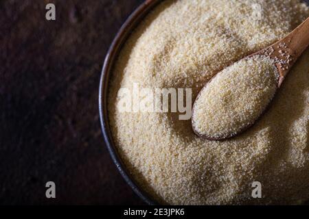 Rohes, unvorbereitetes Grießmehl, auch bekannt als Rava-Pulver in der Schüssel. Rohe unpräparierte Grieß in Schüssel und Löffel Nahaufnahme. Stockfoto