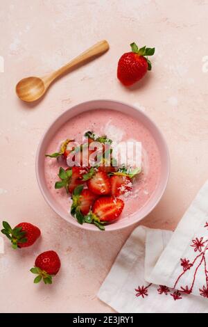 Frühstück mit Müsli, Kokosnuss und Erdbeer Smoothie in einer Schüssel auf einem rosa hellen Hintergrund. Frühling Diät-Menü.Draufsicht. Stockfoto