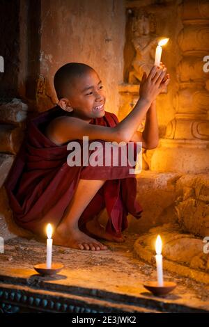 Novize Mönch hält brennende Kerze und lächelt in einem Kerzenschein Tempel, UNESCO, Bagan, Mandalay Region, Myanmar Stockfoto