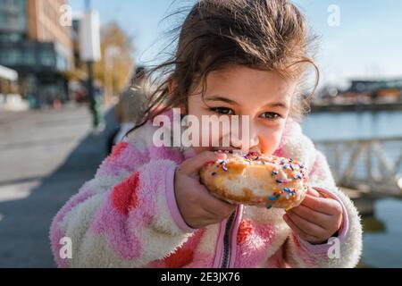 Junges Mädchen essen Donut mit Streuseln draußen Stockfoto