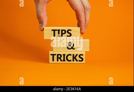 Symbol „Tipps und Tricks“. Holzblöcke mit den Worten "Tipps und Tricks". Schöne orange Hintergrund. Geschäftsmann Hand. Business, Tipps und Tricks Konzept. Stockfoto