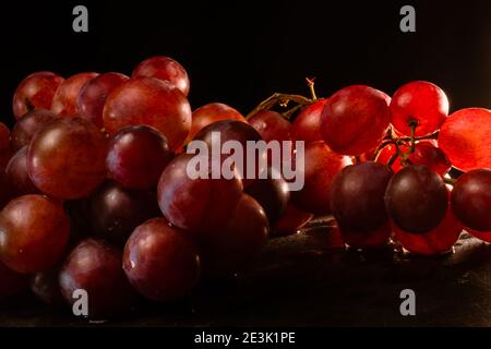 Nahaufnahme von Trauben aus roten Trauben auf einer schwarzen Platte. Intime Beleuchtung. Konzept Delikatesse, Reinheit des Produkts. Selektiver Fokus. Stockfoto