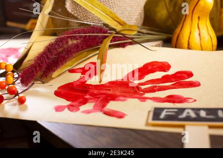 Rote Hand-pute auf Vanille-Baupapier mit orangen Beeren, Herbstlaub und einem 'FALL'-Zeichen Stockfoto