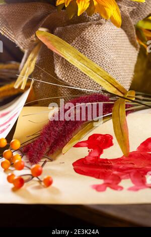 Rote Hand pute auf Vanille-Baupapier mit orangen Beeren Und fallen Laub auf sie und burlap im Hintergrund Stockfoto