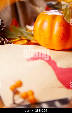 Roter Hand-pute auf Vanille-Baupapier mit orangen Beeren, Kiefernblättern, einem kleinen orangen Kürbis und braunem Laub Stockfoto