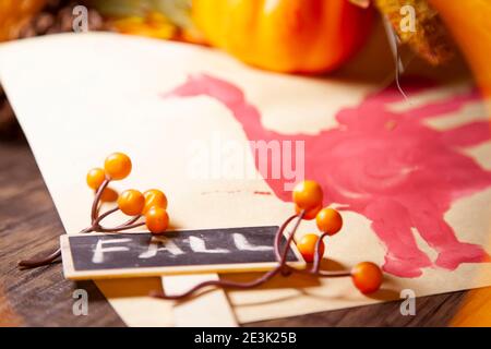 Roter Hand-pute auf Vanille-Baupapier mit orangen Beeren, Kiefernzapfen, einem kleinen orangen Kürbis und braunem Laub mit einem Schild, das 'FALL' n sagt Stockfoto
