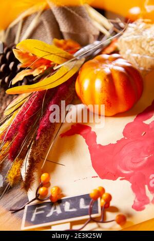 Rote Hand pute auf Vanille-Baupapier mit einem kleinen orangefarbenen Kürbis, braunem und rotem Laub und einem Schild, das 'FALL' darauf sagt Stockfoto