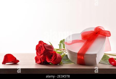 Strauß Rosen und weiße Geschenkbox mit roter Schleife auf Holztisch und weißem Hintergrund isoliert. Vorderansicht. Stockfoto