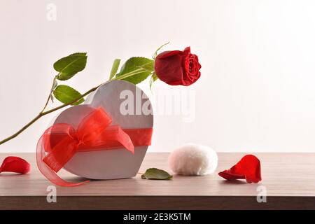 Rose ruht auf Geschenkbox mit Herzform und Blütenblättern auf Holztisch mit isoliertem weißem Hintergrund. Vorderansicht. Stockfoto