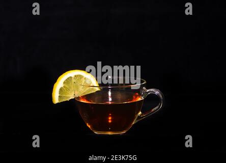 Eine Tasse Tee mit einer gelben Zitronenscheibe Am Rand vor einem schwarzen Hintergrund Stockfoto