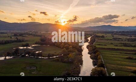 Spektakuläres Luftpanorama des Flusses, der bei Sonnenuntergang durch Felder fließt. Stockfoto