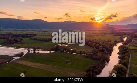 Spektakuläres Luftpanorama des Flusses, der bei Sonnenuntergang durch Felder fließt. Stockfoto