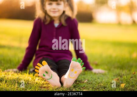 Kind Mädchen mit bemalten Fuß auf grünem Gras Spaß im Freien im Frühling Park. Stockfoto