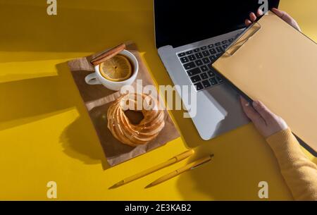 Hände Halten Lebenslauf Blatt in der Nähe Laptop, Kuchen und Tasse Tee auf dem Fortuna Gold Gelb Farbe Hintergrund, Draufsicht. Stockfoto