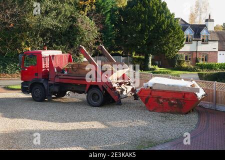 Ein skip-LKW, der einen kompletten skip aus einem Haus sammelt In einer städtischen Straße Stockfoto