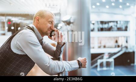 Ein reifer fröhlicher Mann Unternehmer lächelt und mit einem Telefongespräch mit seinem Kollegen, während er sich an den lehnt Balkongeländer ab Stockfoto