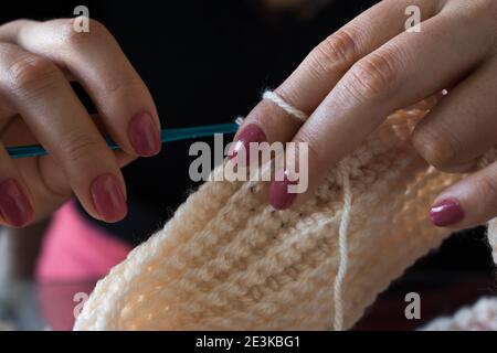 Die Frau strickt Wollkleidung. Stricknadeln. Nahaufnahme der Hände. Arbeiten Sie von zu Hause aus. Naturwolle. Stockfoto