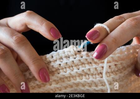 Die Frau strickt Wollkleidung. Stricknadeln. Nahaufnahme der Hände. Arbeiten Sie von zu Hause aus. Naturwolle. Stockfoto