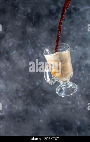 Kaffee mit Milch und Cookies in Form von Herzen. Der Prozess des Gießen von Kaffee in ein Glas Milch. Levitation Stockfoto